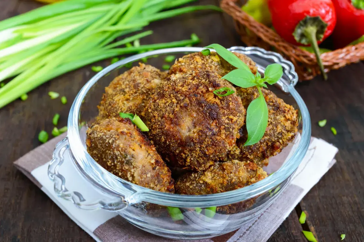 Chrupiące mielone z pieczarkami w szklanej misie, ozdobione listkami bazylii i szczypiorkiem. Obok pęczek zielonej cebulki i czerwone papryczki.
