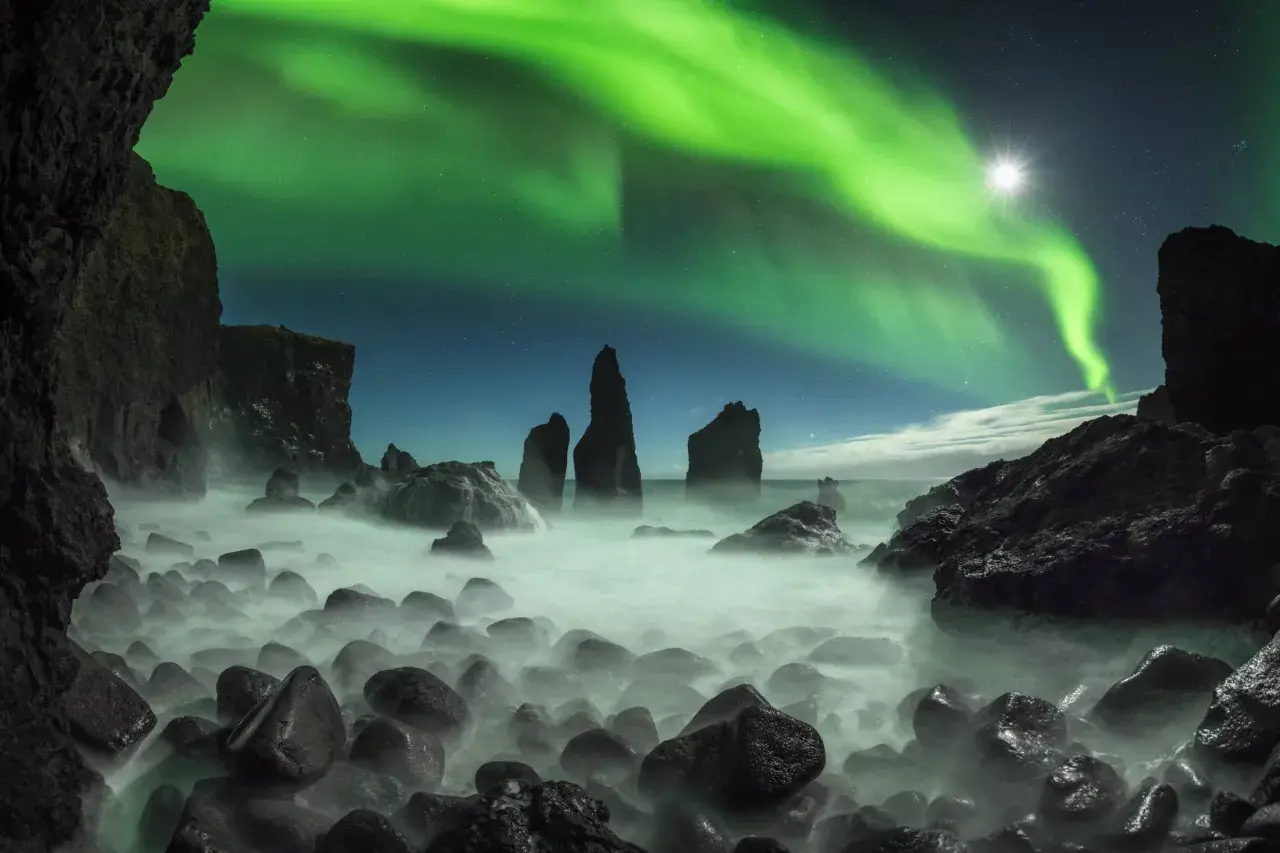 Grüne Nordlichter tanzen über einer felsigen Küste. Ein magischer Septemberabend auf einer Insel, wo das Meer in Nebel gehüllt ist.