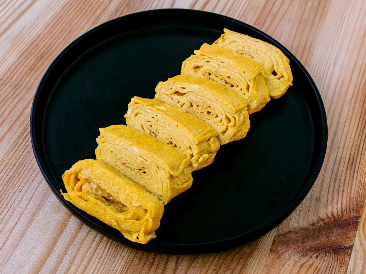 Tranches d'oeuf tamago, un délice japonais, disposées sur une assiette noire.