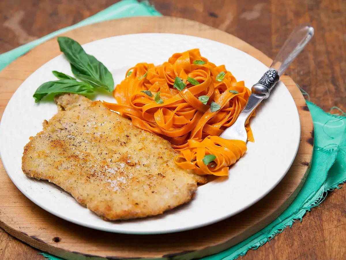 Escalope de veau panée, servie avec des tagliatelles de carottes et des feuilles de basilic. Une recette simple et savoureuse.