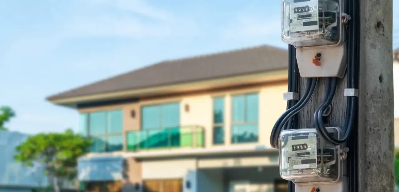 Medidores de luz, sensores eléctricos, en un poste frente a una casa moderna.