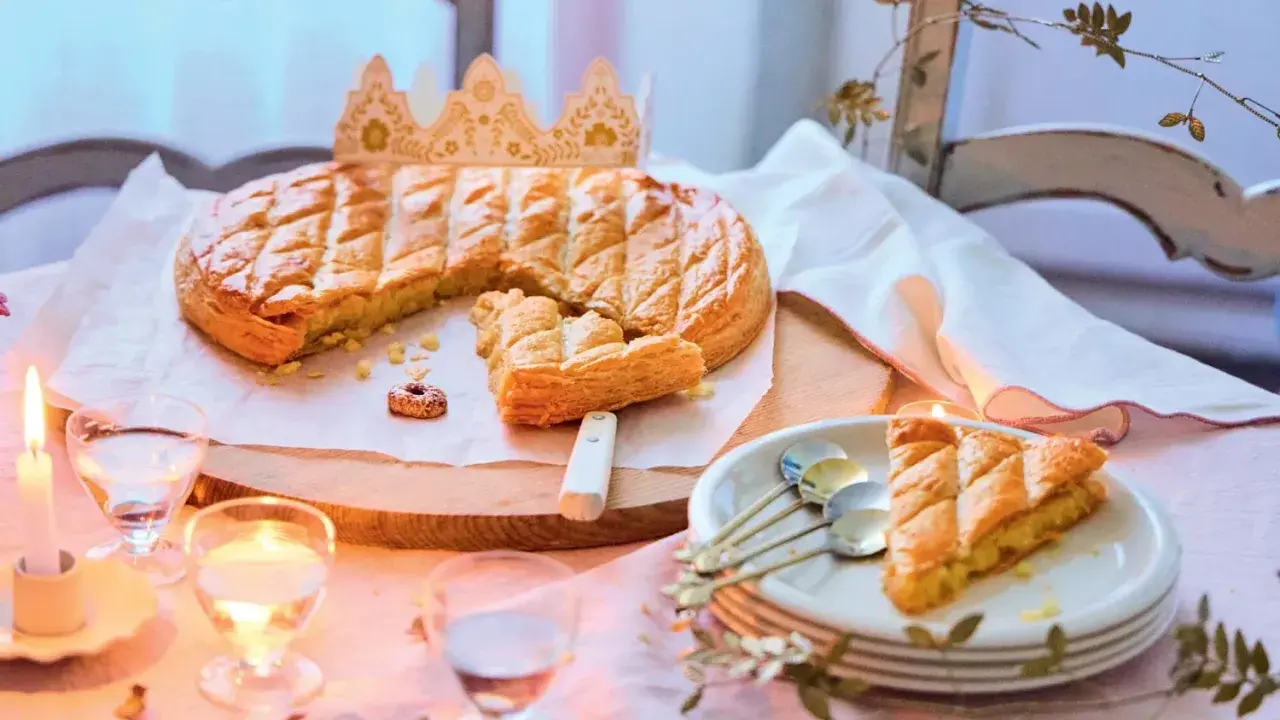 Une galette des rois dorée, prête à être partagée, avec une couronne posée à côté. Une part est déjà servie, invitant à la fête.