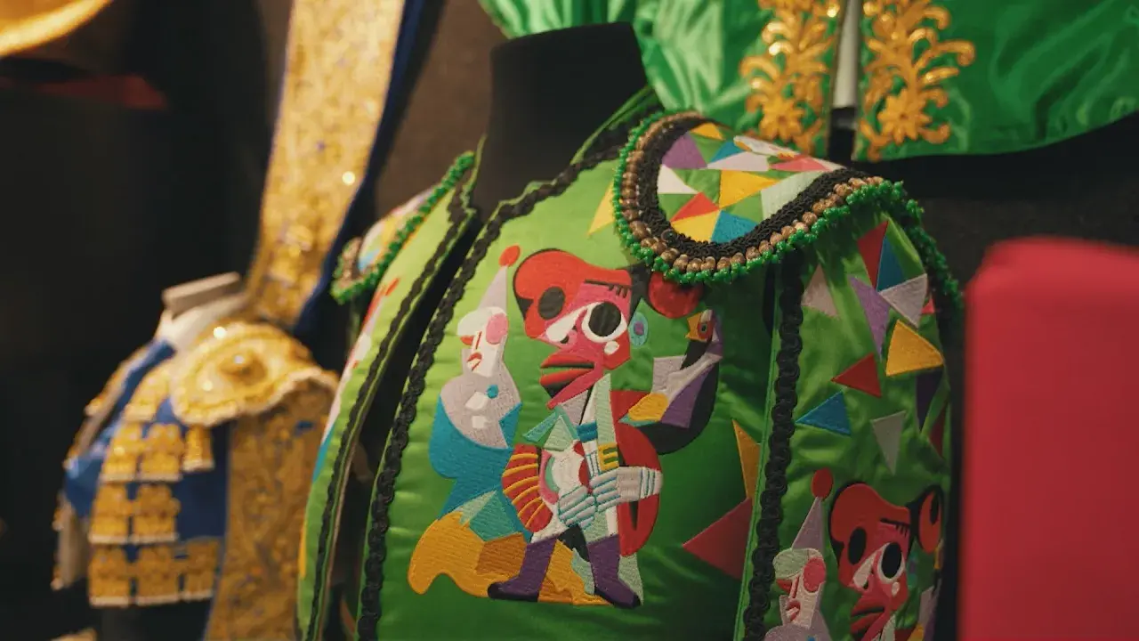 Detalle de coloridos bordados en partes del traje de torero, con figuras abstractas y geométricas sobre fondo verde.