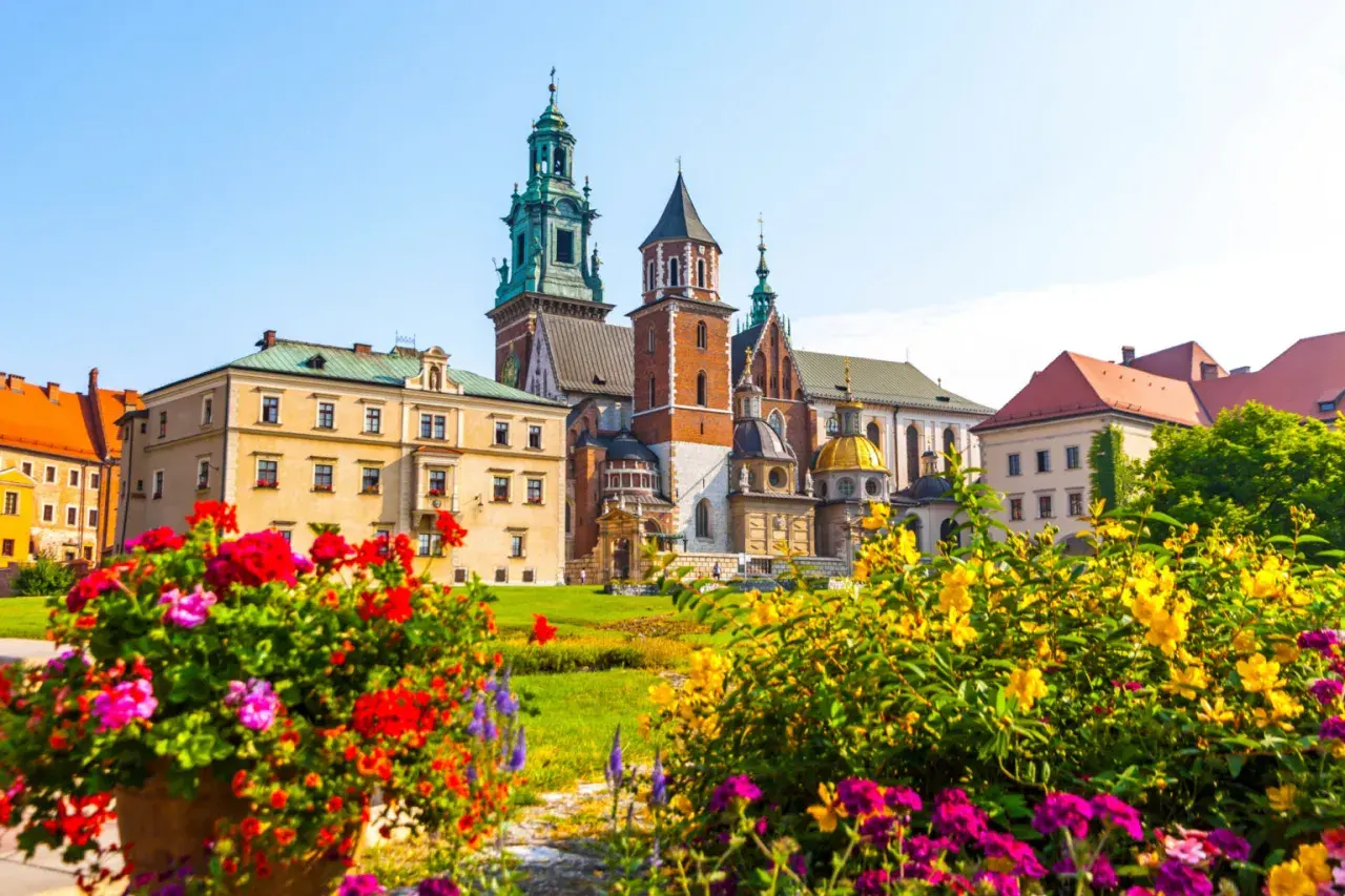 Krakowski Wawel, wpisany na **UNESCO listę polską**, w otoczeniu kwitnących kwiatów.