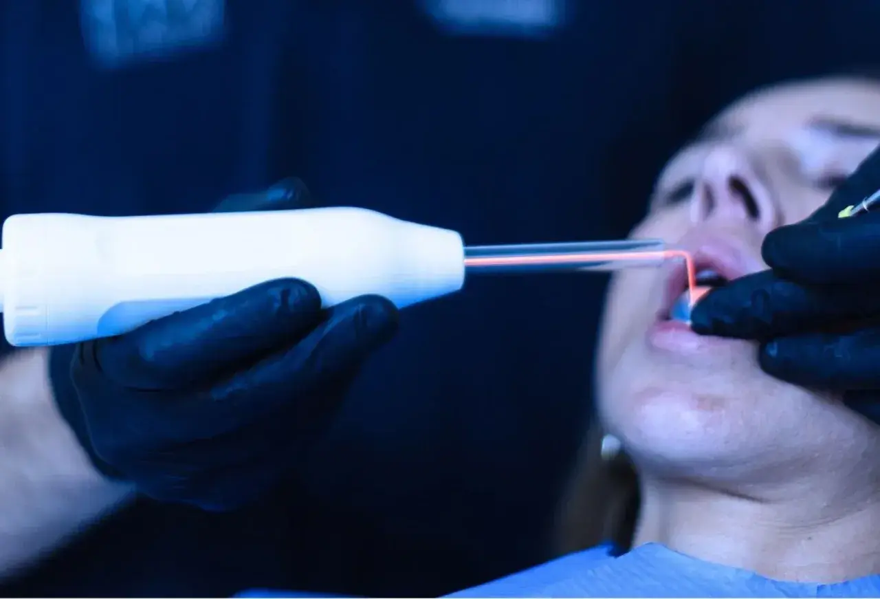 Trattamento laser per come rinforzare le gengive. Un professionista usa uno strumento con luce rossa su una bocca.