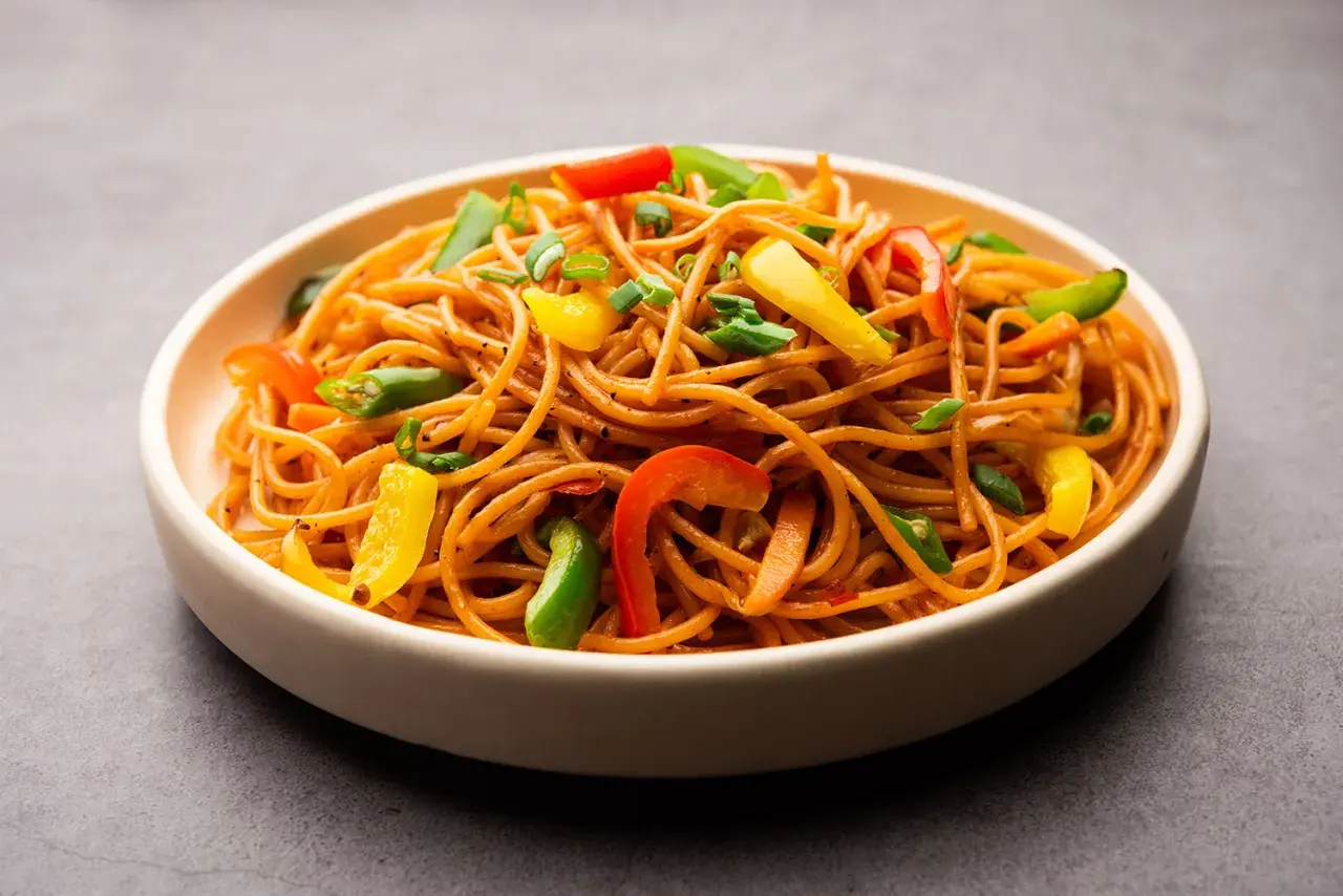 Un plato de espaguetis con verduras salteadas, con pimientos de colores y cebolleta.
