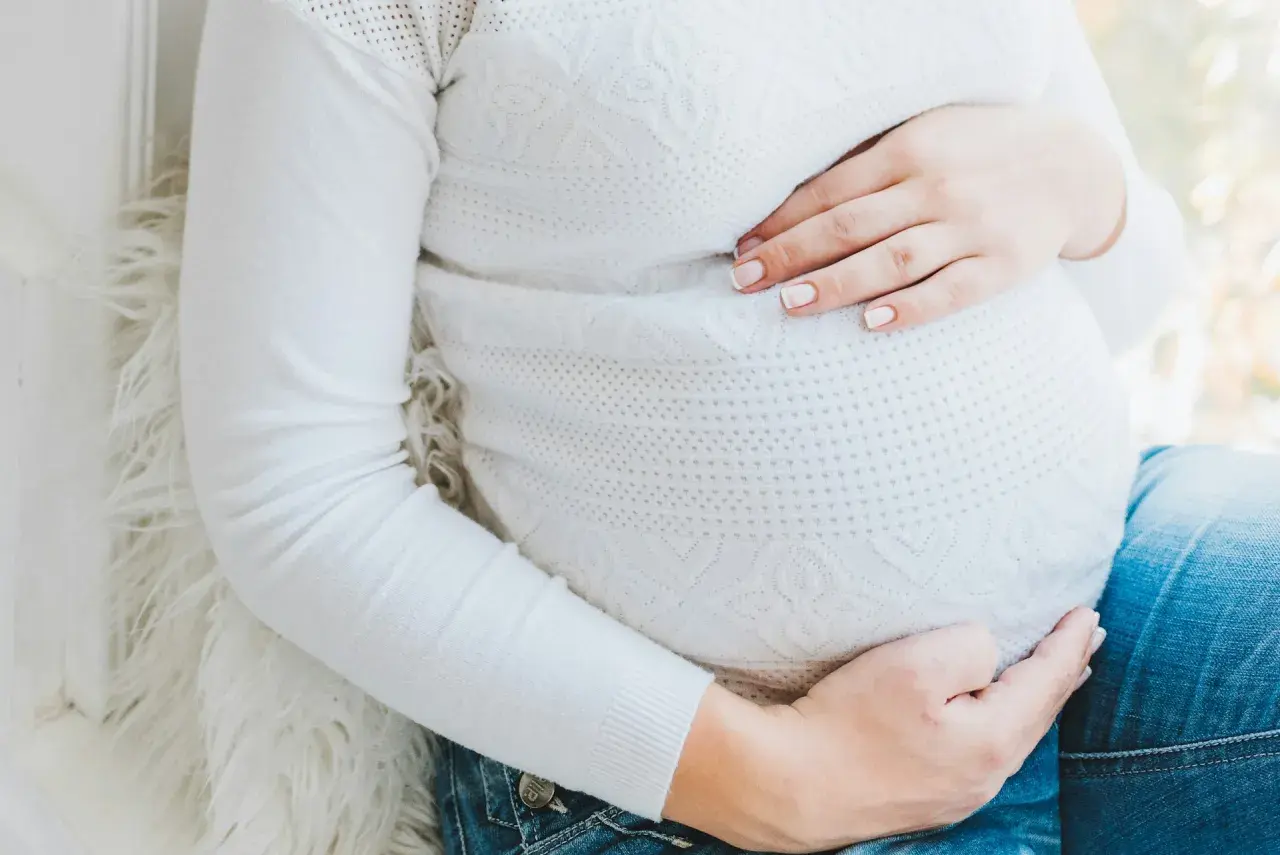 Gravid mage med händer som vilar på den. Kanske känner hon av ont i blygdbenet gravid.