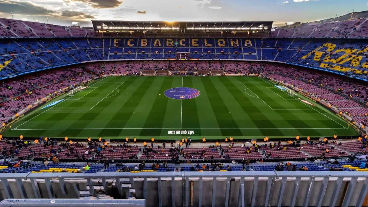Widok na murawę i trybuny stadionu FC Barcelona Camp Nou. Słońce zachodzi nad stadionem.