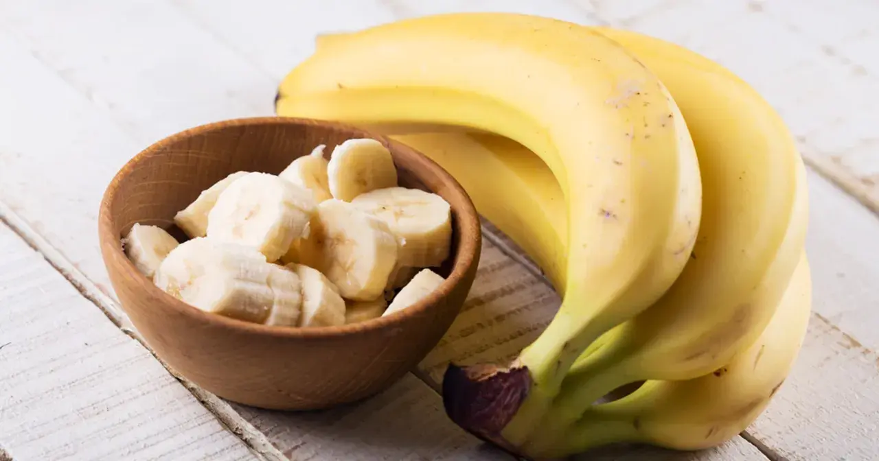 Dojrzały banan kcal w miseczce i pęczek bananów na drewnianym stole.