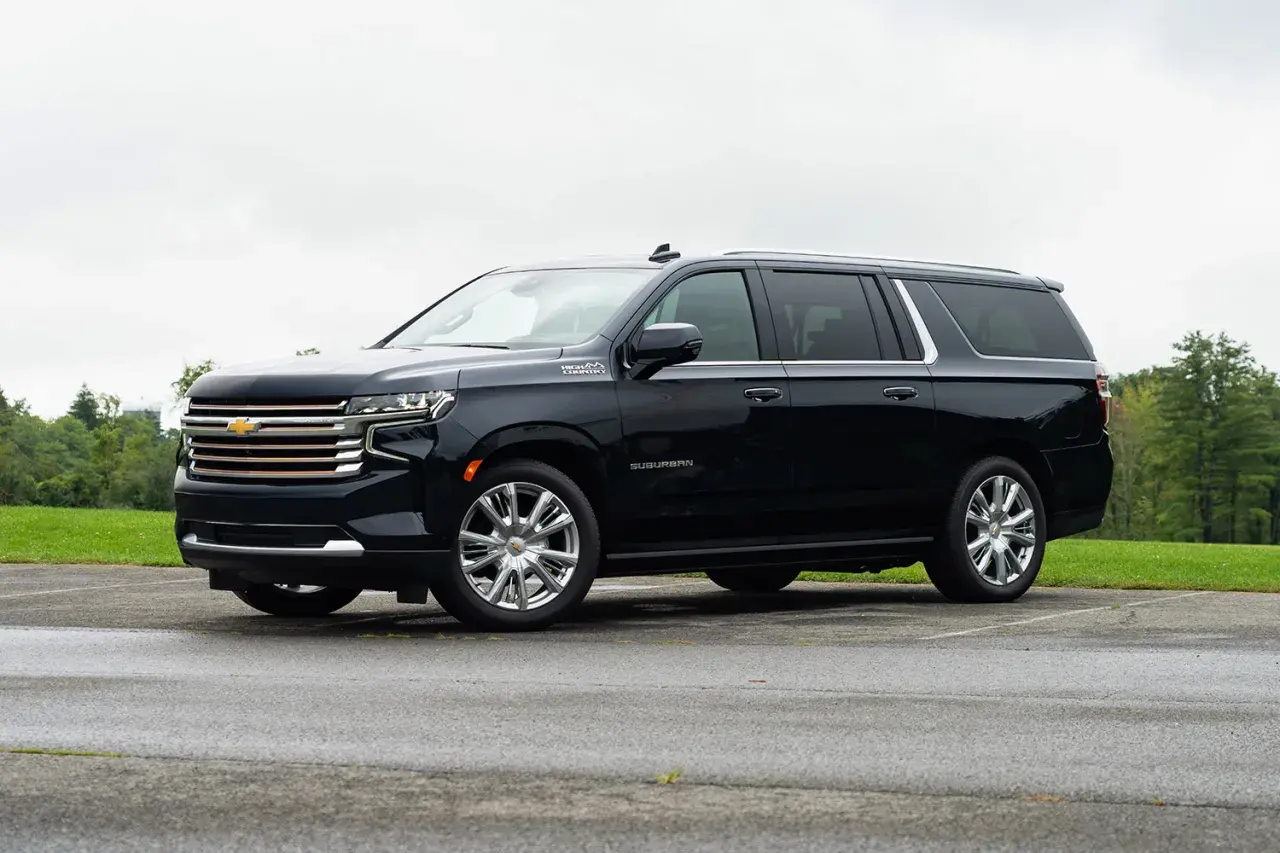 Czarny Chevrolet Suburban High Country z chromowanymi felgami stoi na mokrym parkingu, otoczony zielenią.