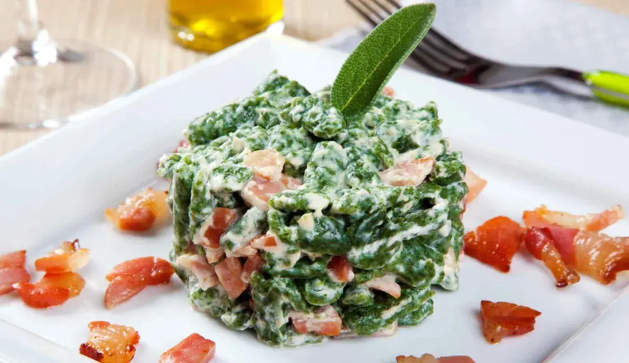 Spätzle verdi cremosi con pezzetti di speck croccante, guarniti con una foglia di salvia. Un piatto invitante.