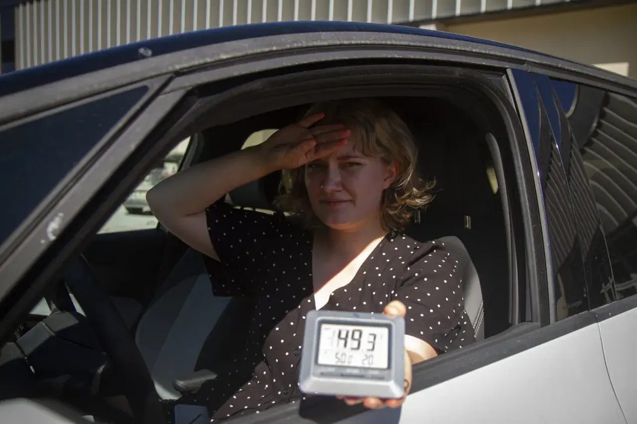 Kvinna i bil svettas och håller upp en termometer som visar 49,3 grader. Det är så varmt att bilen blir inte varm.