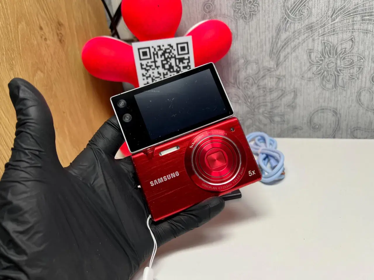 Czerwony aparat Samsung MV800 z obracanym ekranem, trzymany w czarnej rękawiczce.