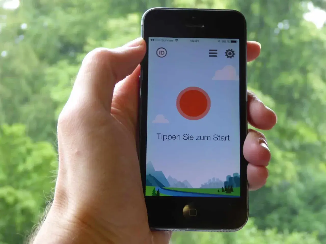 Ein Smartphone wird gehalten, um Vogelstimmen vorspielen zu lassen. Die App zeigt eine Landschaft und den Text "Tippen Sie zum Start".