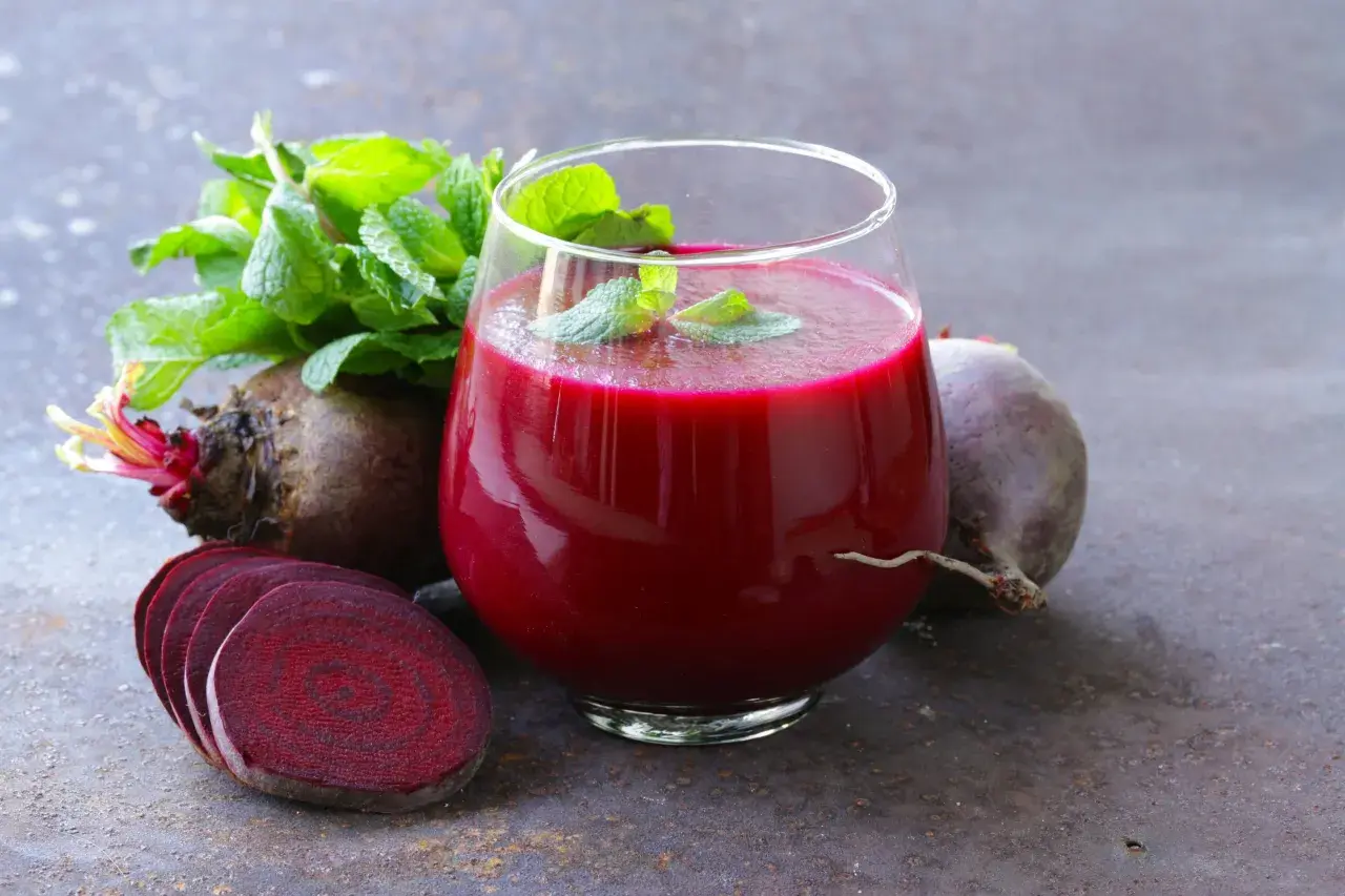 Ein Glas tiefroter Rote Bete Saft, garniert mit Minze, neben frischen Rote Bete Knollen und Scheiben. Ein natürlicher Booster für Vitalität und eine gesunde Erektion.
