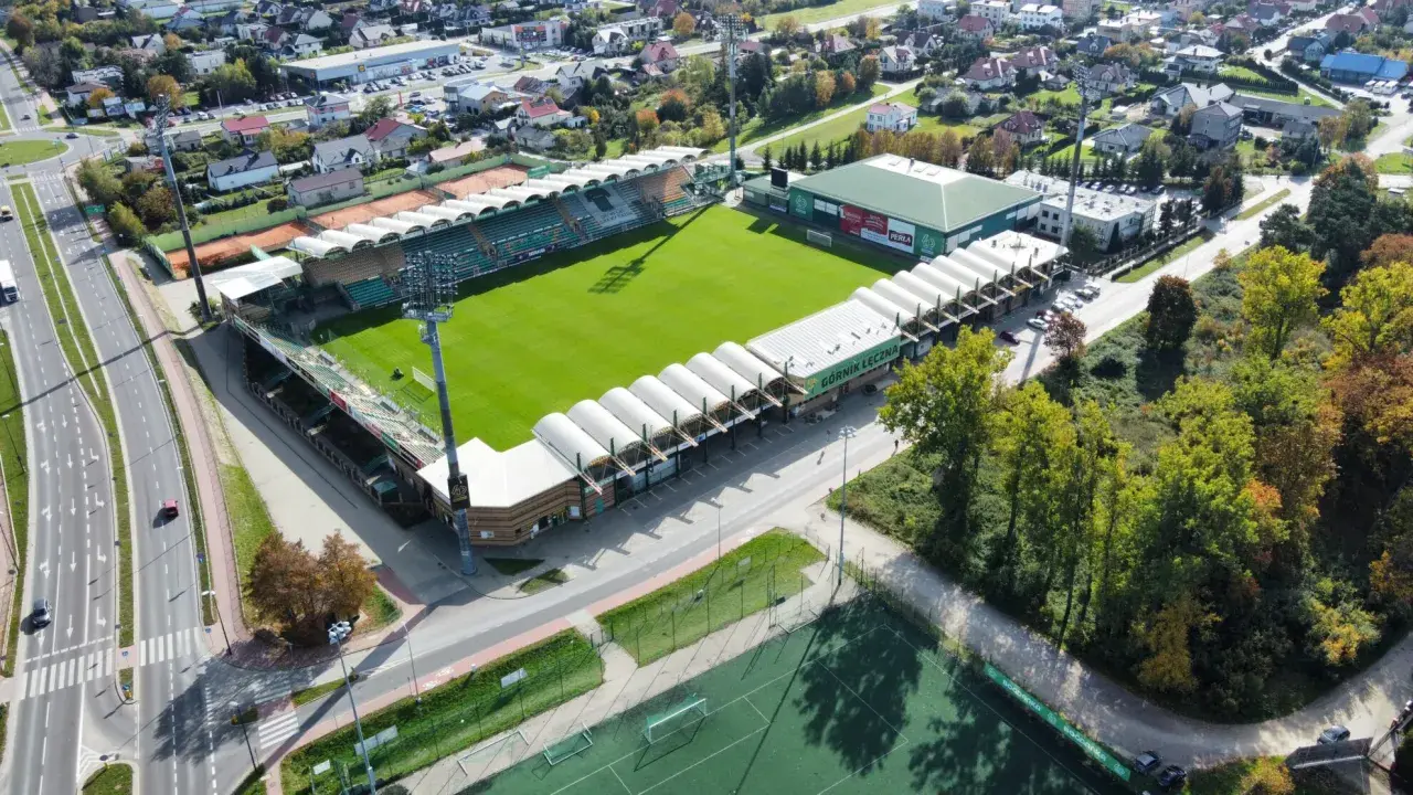 Widok z lotu ptaka na stadion Górnik Łęczna z zieloną murawą, trybunami i otaczającymi go budynkami.
