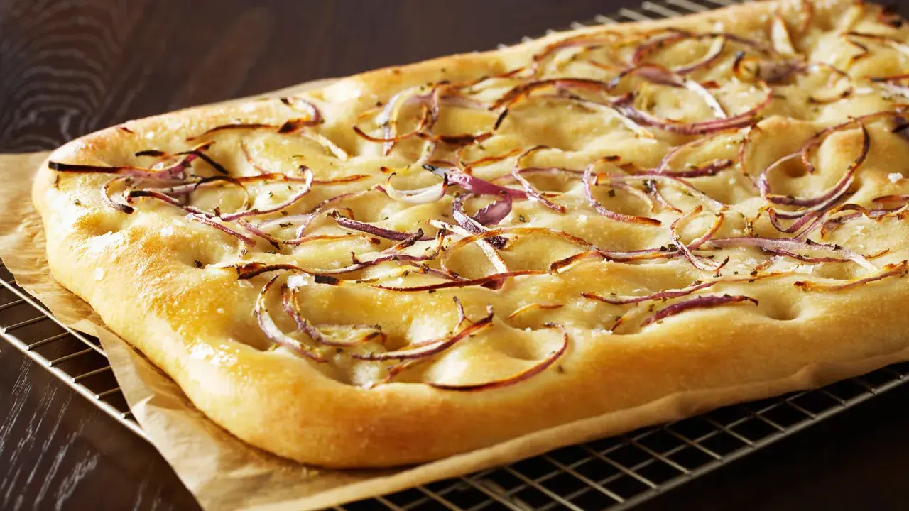 Focaccia dorada con finas rodajas de cebolla balsámica y sal gruesa, recién salida del horno.