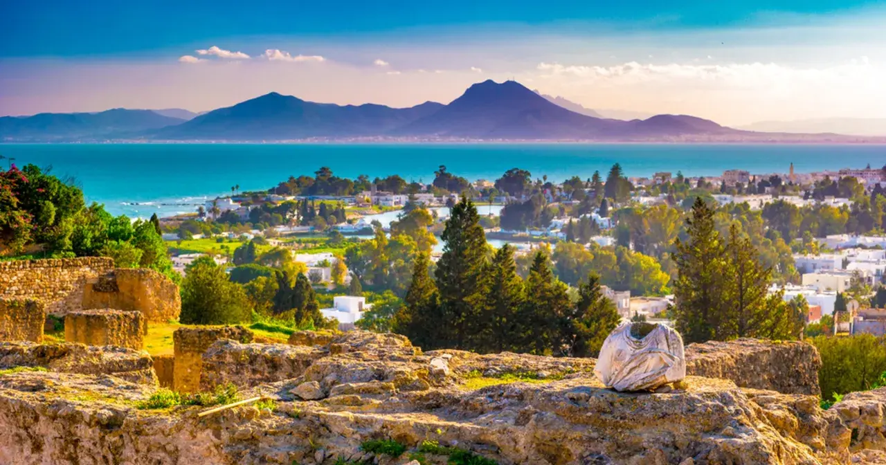 Tunis, afrykańska stolica nad Morzem Śródziemnym, rozciąga się od starożytnych ruin po białe domy, z górami w tle.