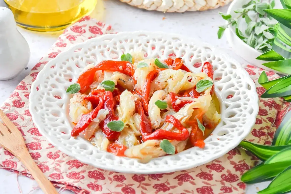 Deliciosa ensalada de bacalao con pimientos rojos asados y hierbas frescas, servida en un plato blanco decorado.