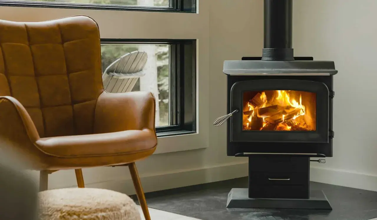 Un confortable fauteuil en cuir brun fait face à un poêle à bois non étanche, où des flammes dansent joyeusement dans le foyer.