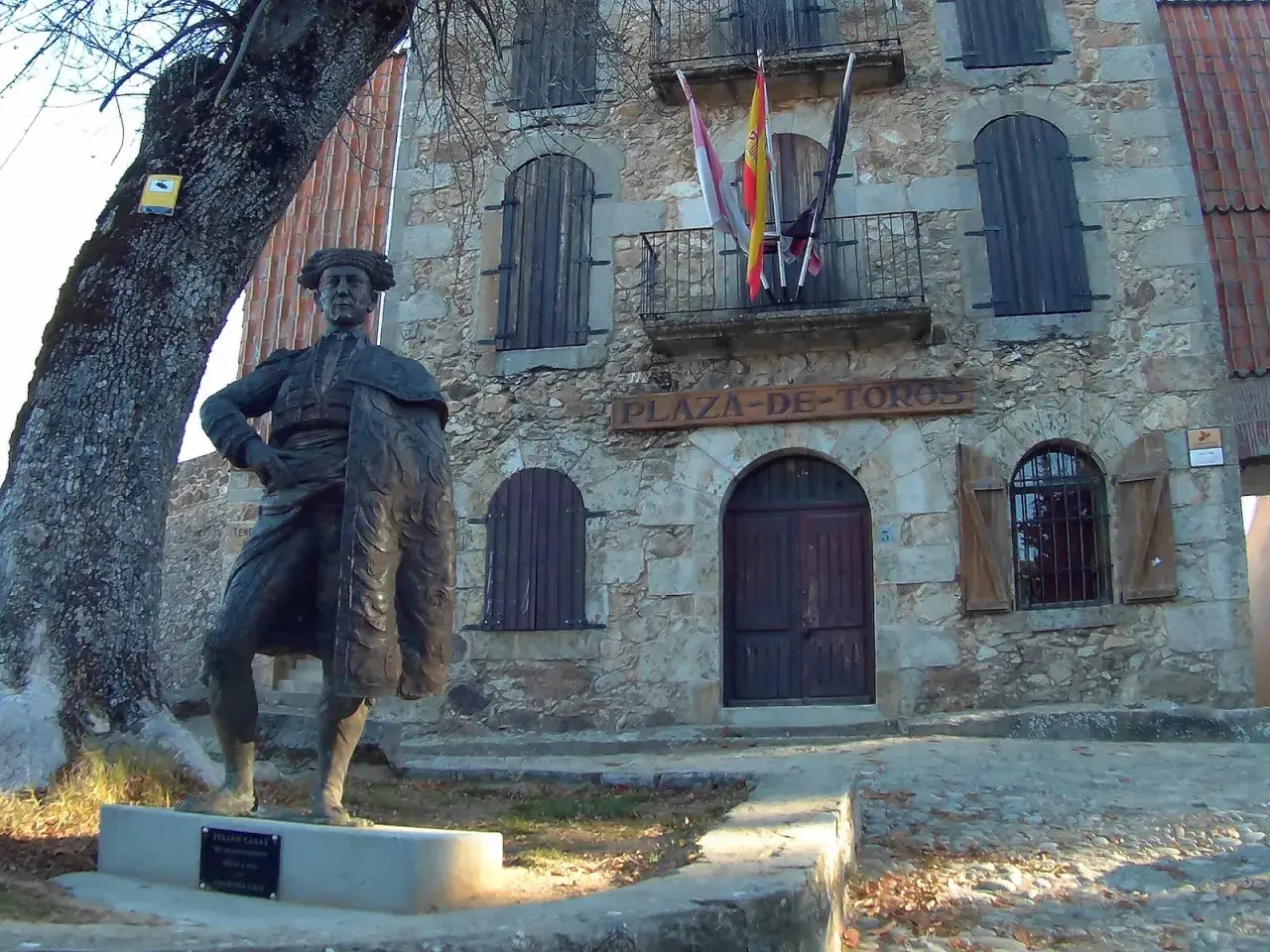 Estatua de un torero frente a la plaza de toros la ancianita. El edificio de piedra tiene un letrero y banderas españolas.