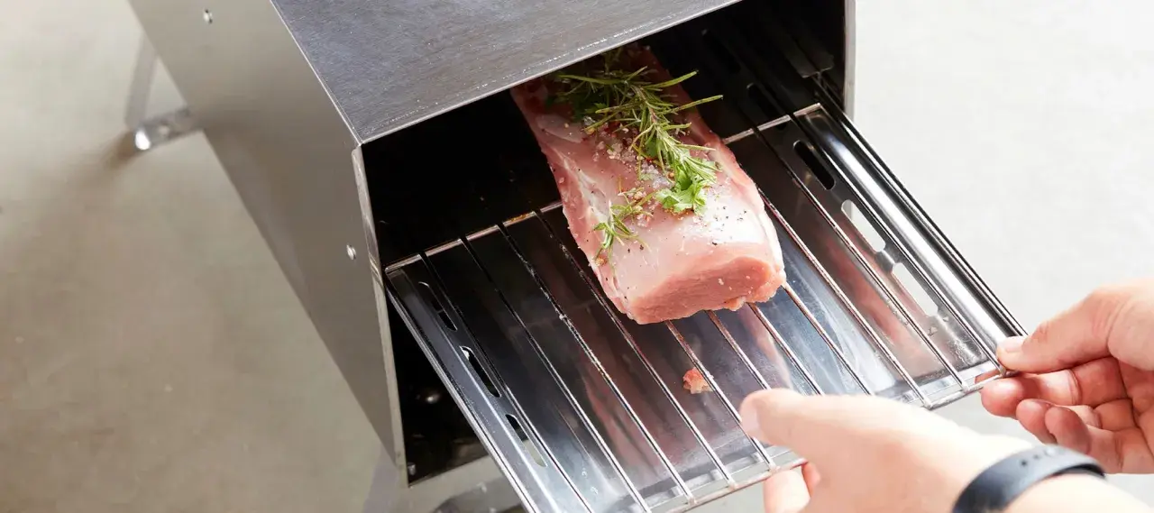 Un filet mignon fumé prêt à être cuisiné, assaisonné d'herbes et de poivre, est placé dans un fumoir. Une recette savoureuse en perspective.