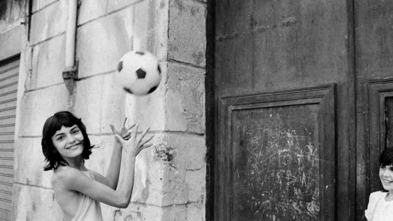 Letizia Battaglia giovane gioca con un pallone, un'immagine che cattura la spensieratezza dell'infanzia.