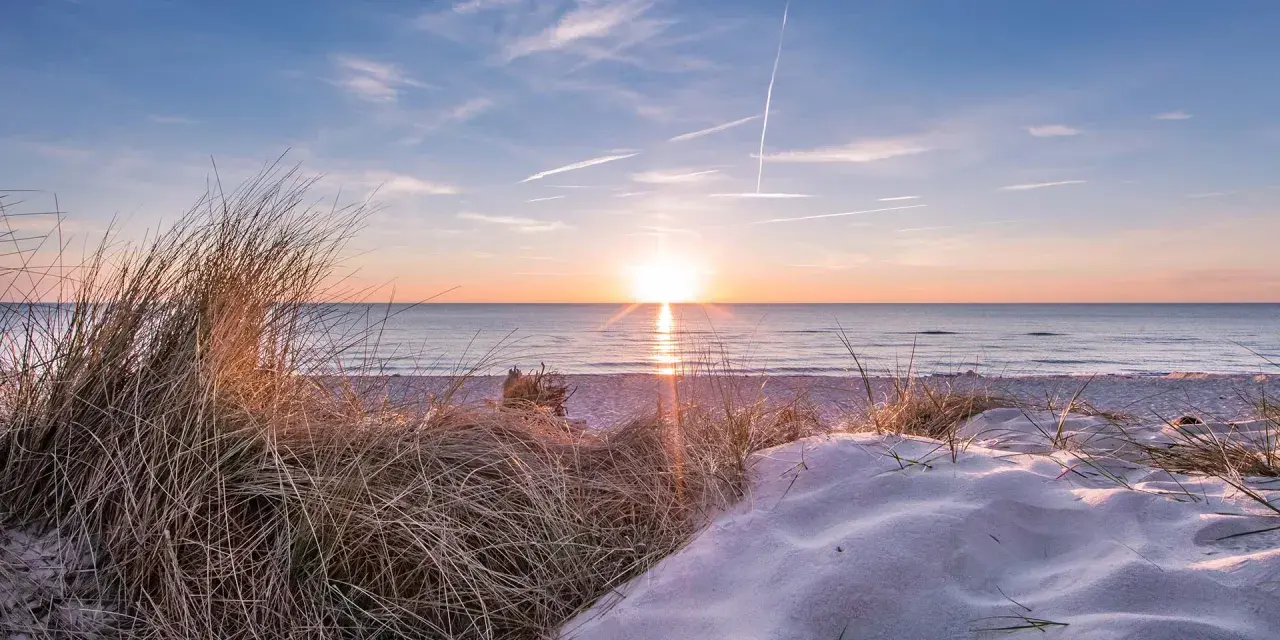 Sonnenuntergang am Strand, ein perfekter Urlaub in Deutschland. Dünen mit Gräsern und Sand, das Meer glitzert.