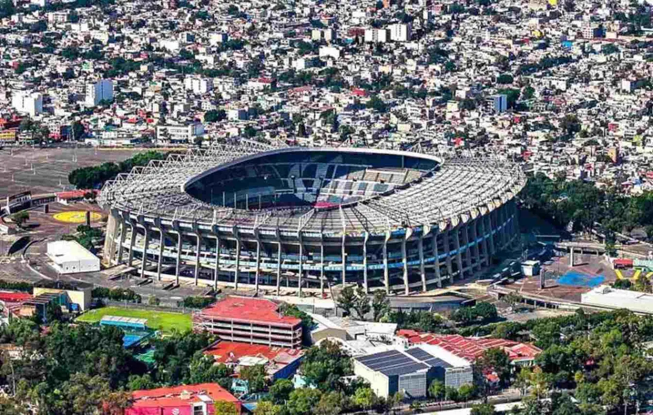 Widok z lotu ptaka na monumentalny stadion Azteca otoczony gęstą zabudową miejską.