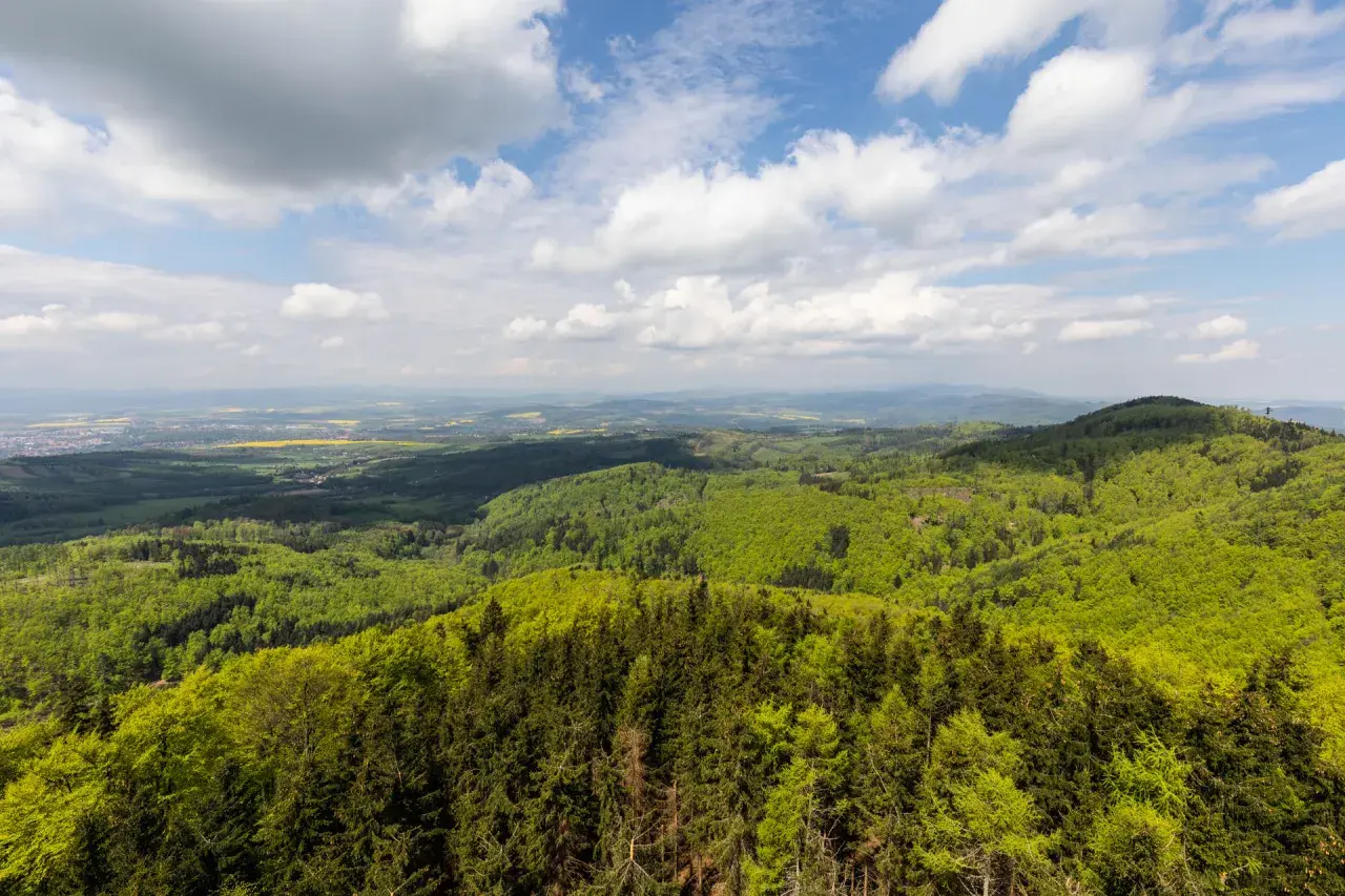 Widok z Kłodzkiej Góry na zielone wzgórza i pola. Niebo z chmurami.