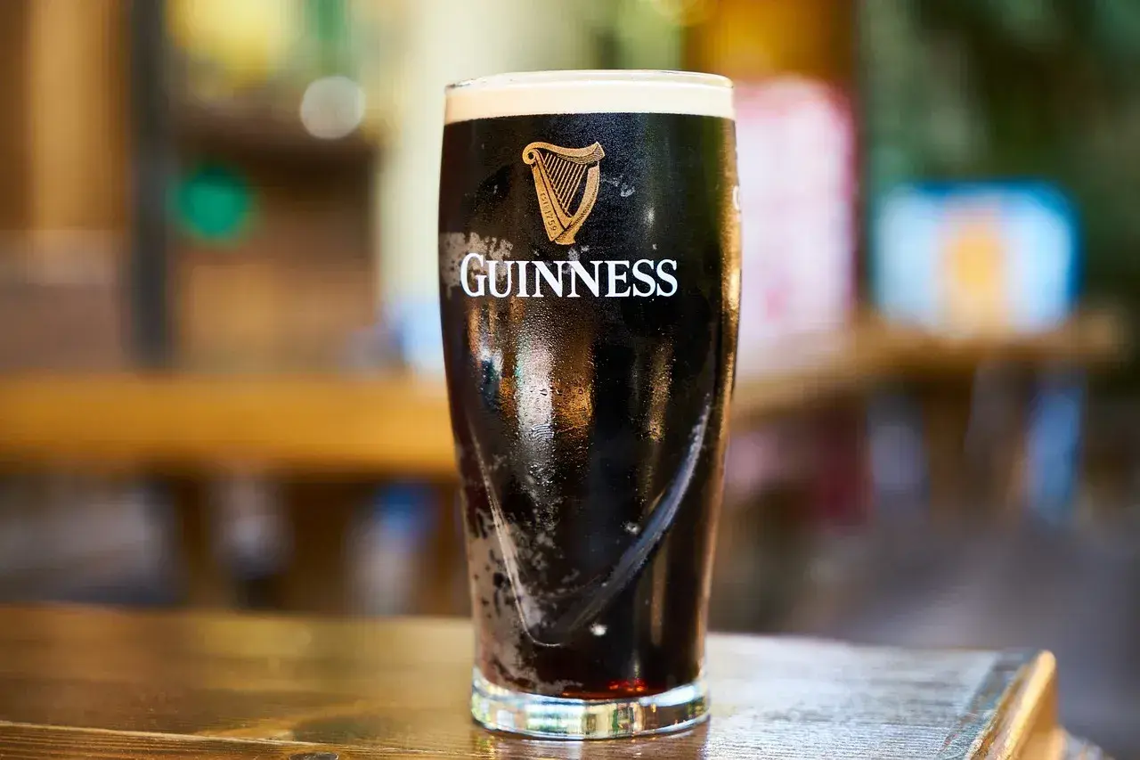 Szklanka z ciemnym piwem słodowym Guinness, z charakterystycznym logo harfy i napisem. Piana tworzy grubą warstwę.