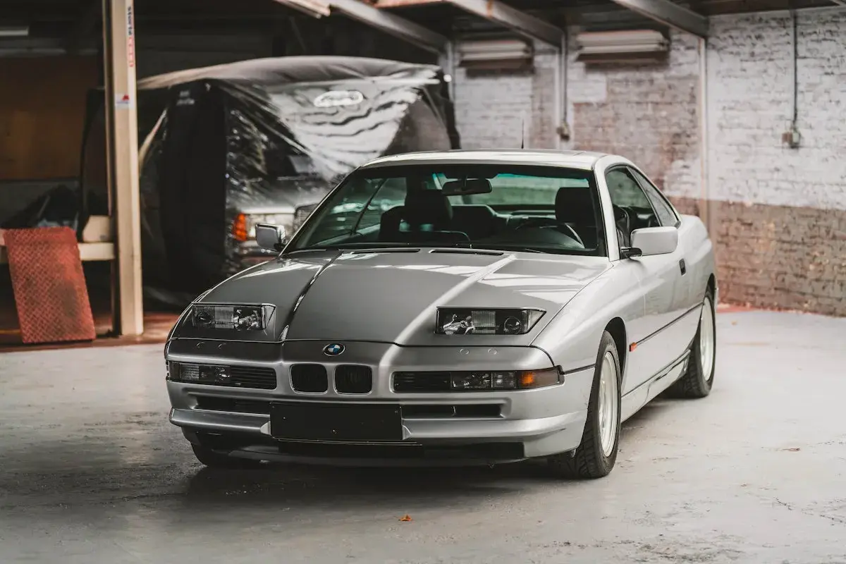 Un elegante BMW E31 plateado, un clásico deportivo, descansa en un garaje con paredes de ladrillo.
