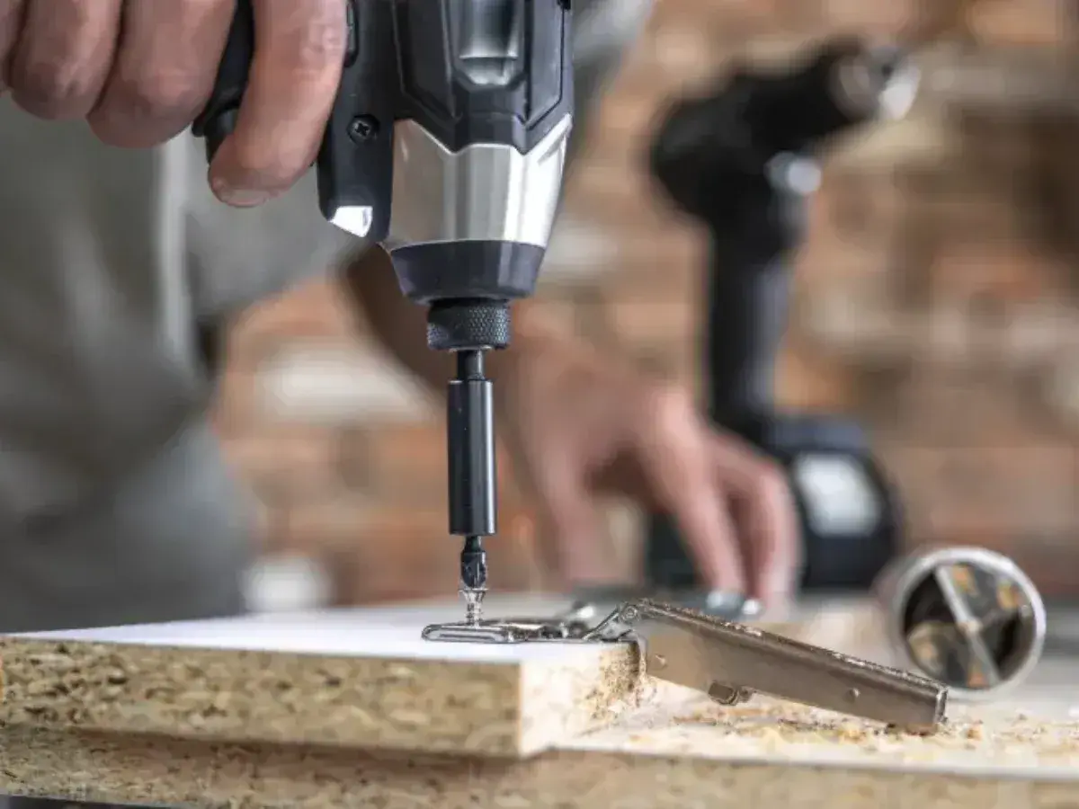 Instrucciones sobre como poner una broca en un taladro. Un hombre usa un taladro para fijar una bisagra a un tablero de madera.