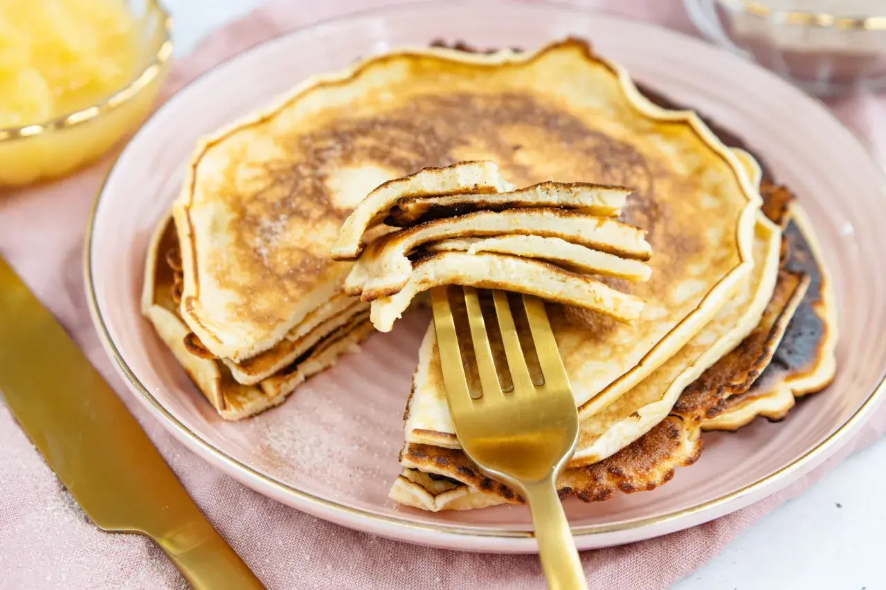 Ein goldener Löffel hebt einen Stapel fluffiger Pfannkuchen an. Dieses Pfannkuchen Rezept von Oma ist ein Genuss!