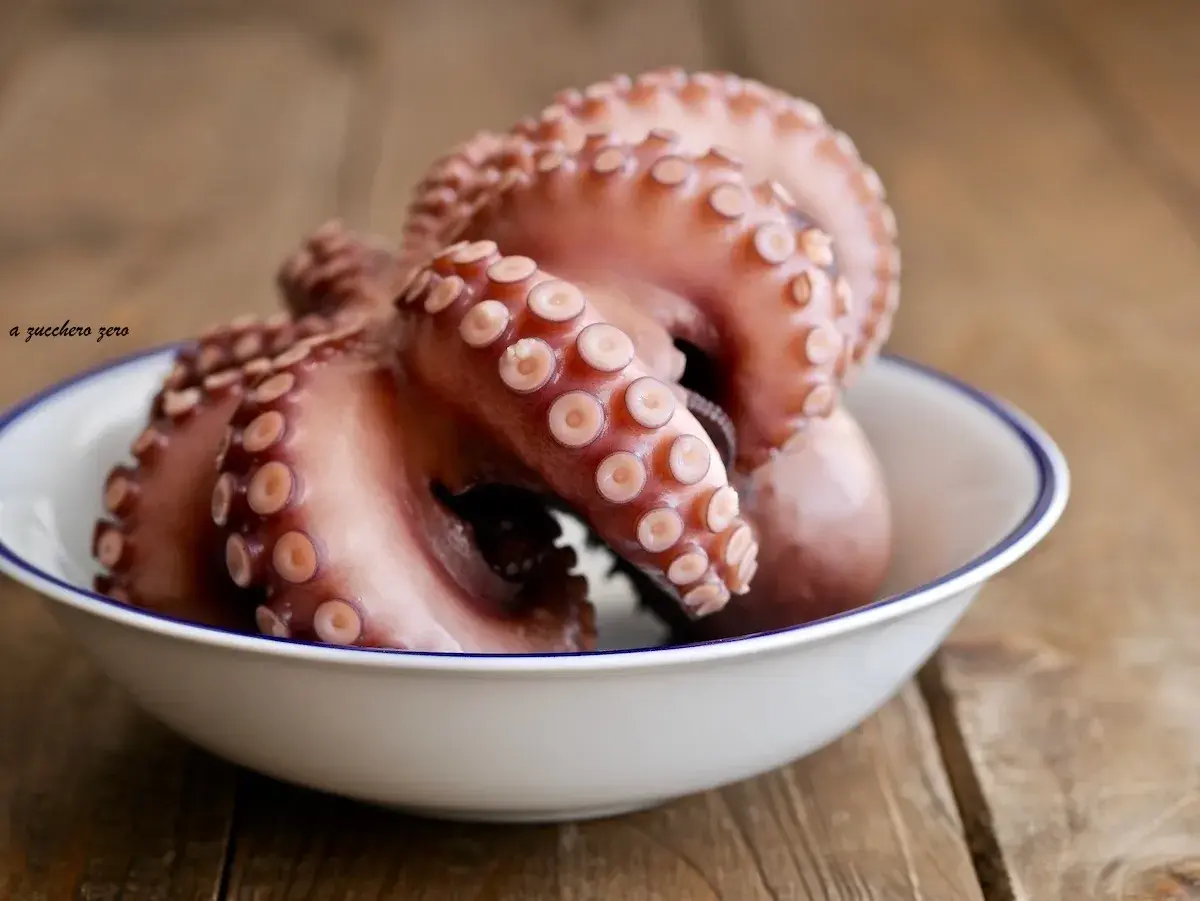 Un poulpe cuit, prêt pour une délicieuse recette. Ses tentacules aux ventouses sont mis en valeur dans un bol blanc sur fond de bois.