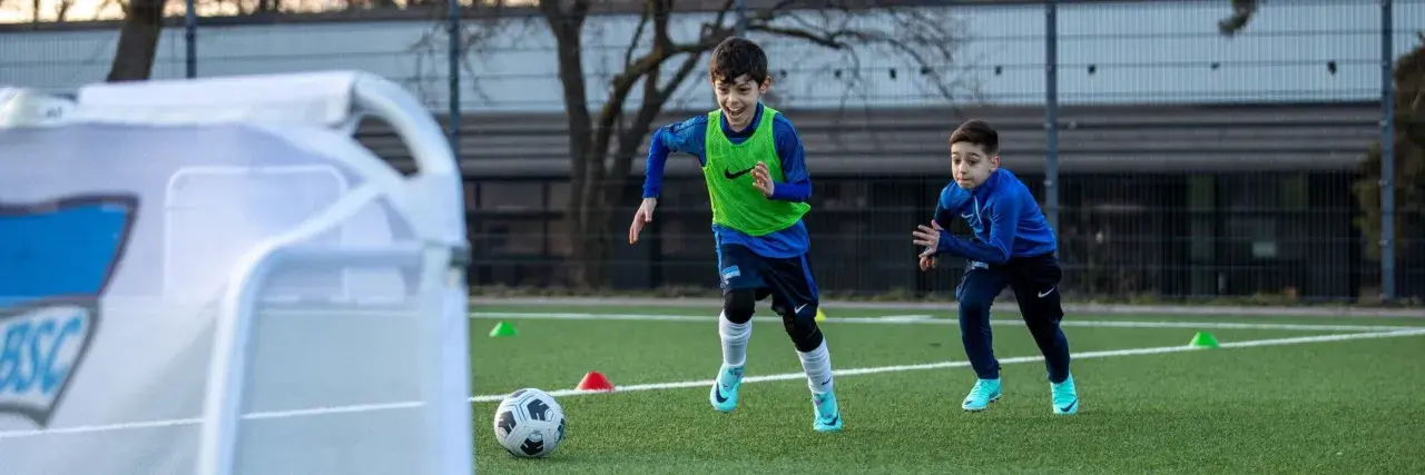 Zwei Jungen in Fußballtrikots trainieren auf einem Kunstrasenplatz. Sie sind voller Energie und Freude, während sie über das Feld rennen. Diese fussball spiele kinder sind ein toller Anblick!
