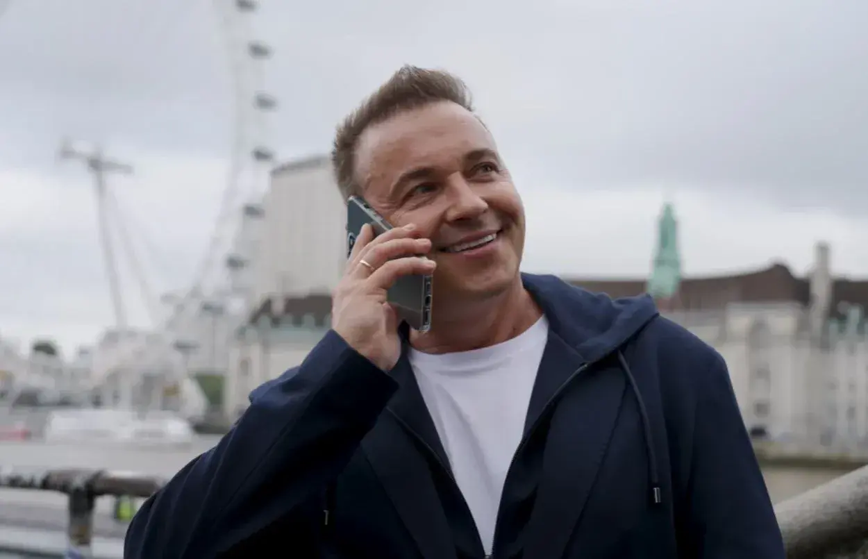 Uśmiechnięty mężczyzna rozmawia przez telefon. W tle widać London Eye. Weekend, halo, tu Londyn!