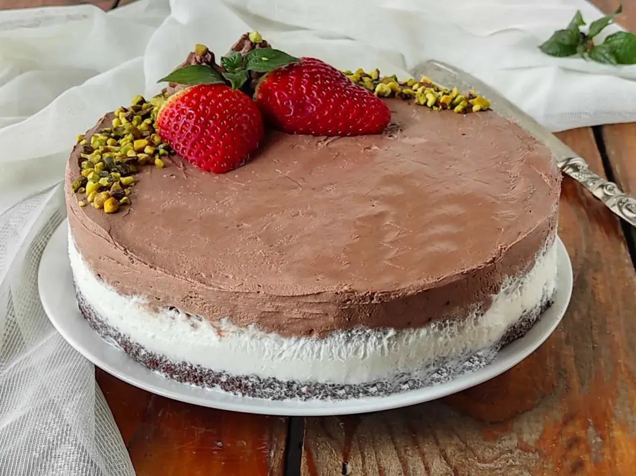 Deliziosa torta al gelato al cioccolato e panna, decorata con fragole, pistacchi e menta.