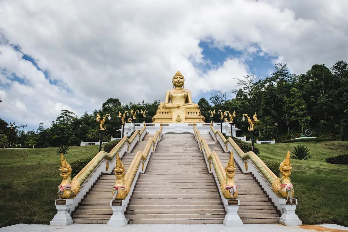 Goldene Buddha-Statue über einer langen Treppe mit Naga-Schlangen-Geländern in Nakhon Si Thammarat.