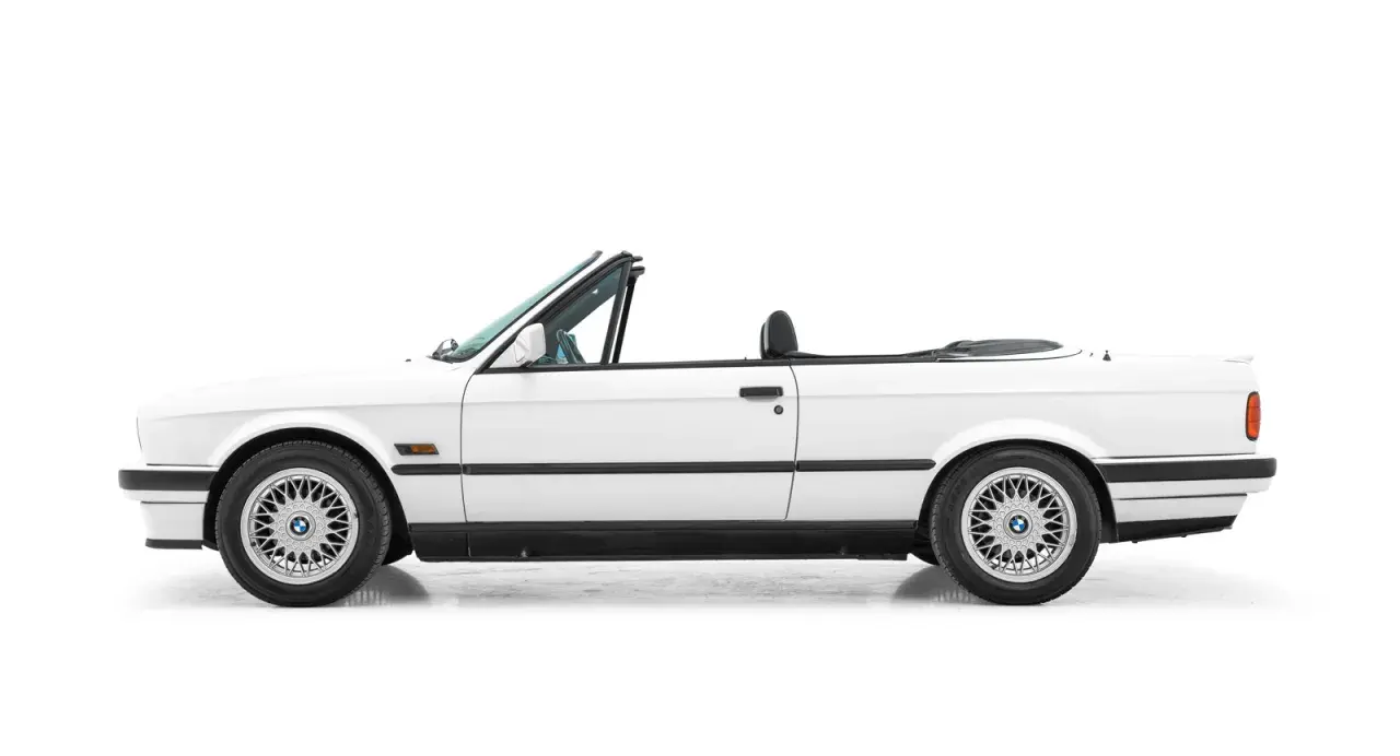 Vit cabriolet, en klassisk bmw 80 tal, med taket nere. Perfekt för sommarvägar.