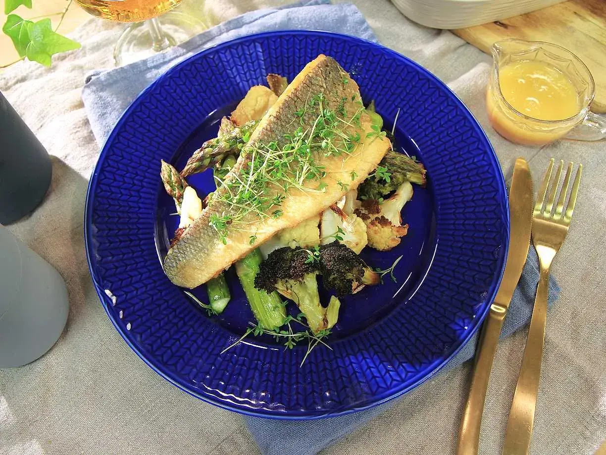 En läcker havsabborre med rostade grönsaker, perfekt för ett enkelt havsabborre recept. Serveras med en ljus sås och gyllene bestick.
