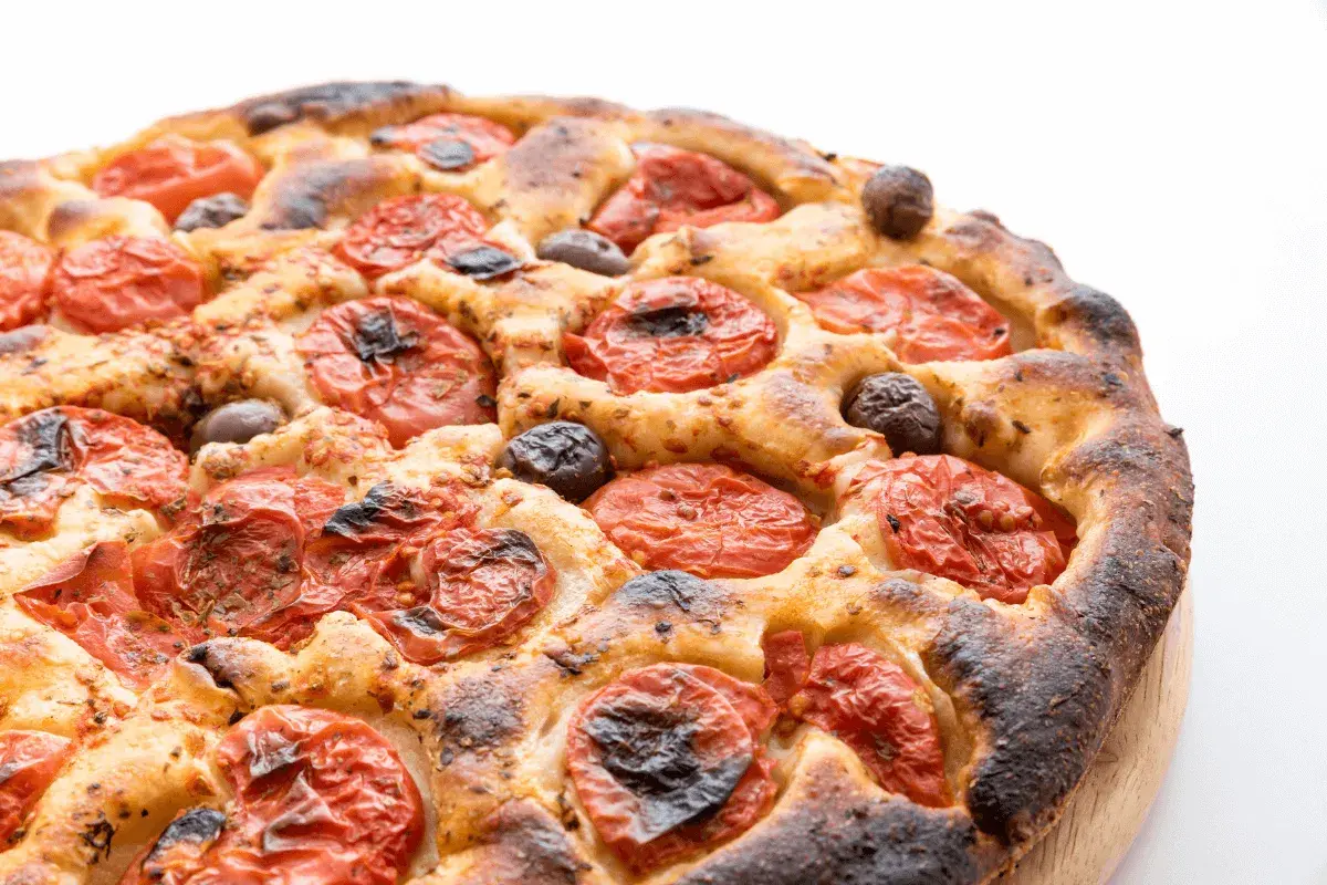 Focaccia barese dorata e fragrante, con pomodorini succosi e olive nere, pronta per essere gustata.