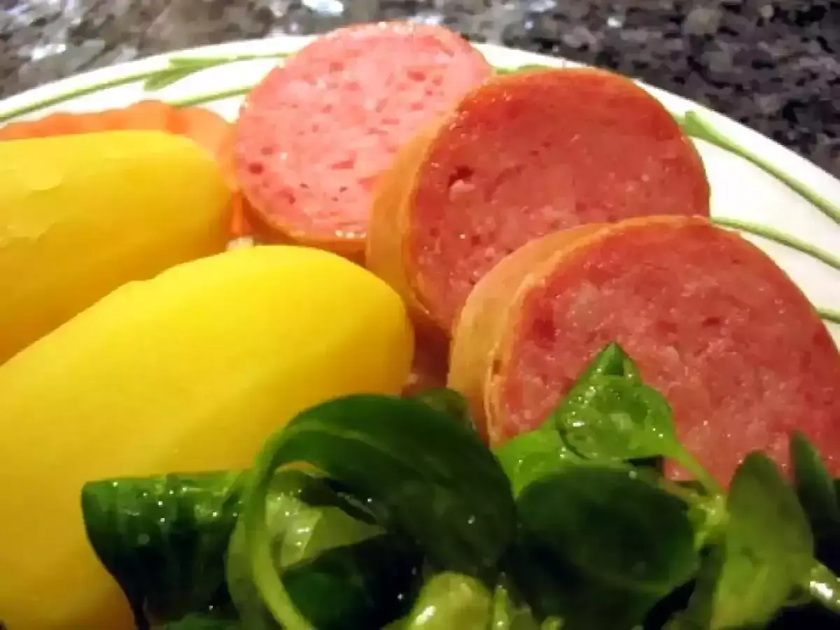 Tranches de saucisson savoureux accompagnées de pommes de terre jaunes et d'une salade verte fraîche.