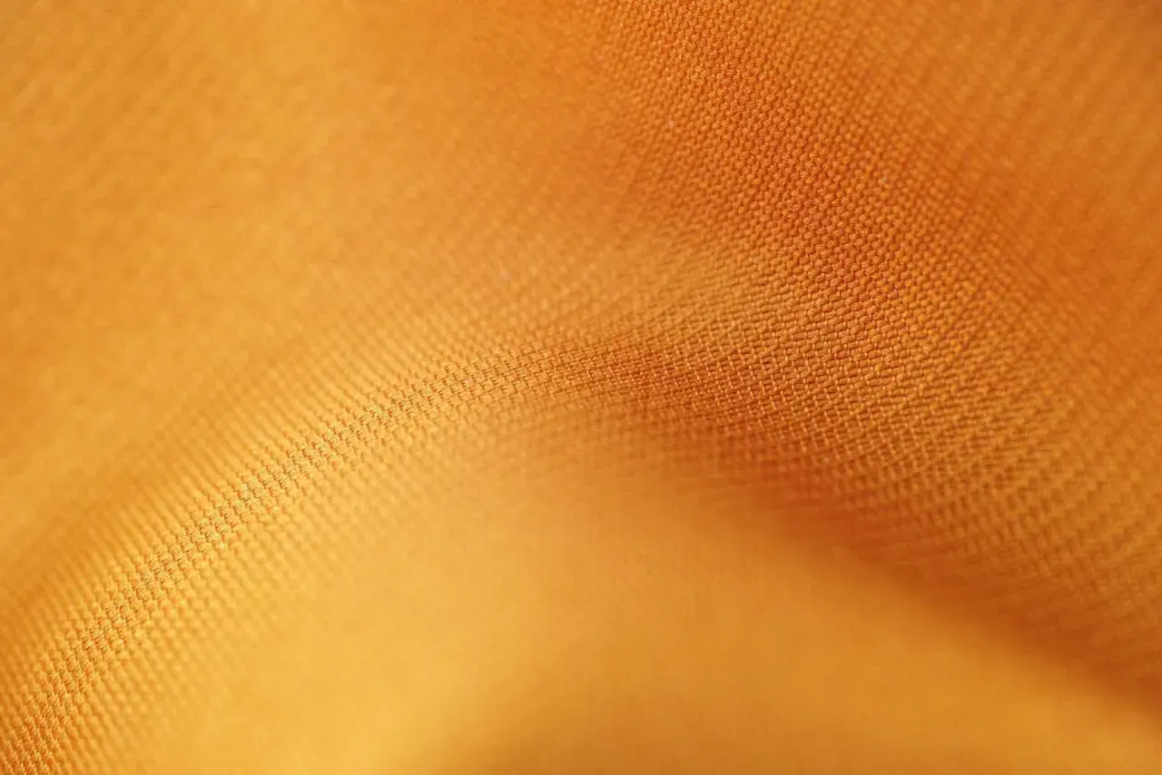 Texture d'un tissu orange vif, où chaque rayon fibre est visible, créant un motif subtil et doux.