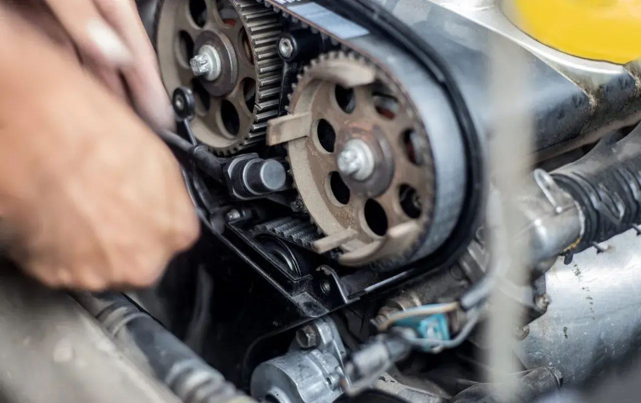 Meccanico lavora sul motore, sostituendo la cinghia di distribuzione. Il costo di questa operazione è importante per la manutenzione.