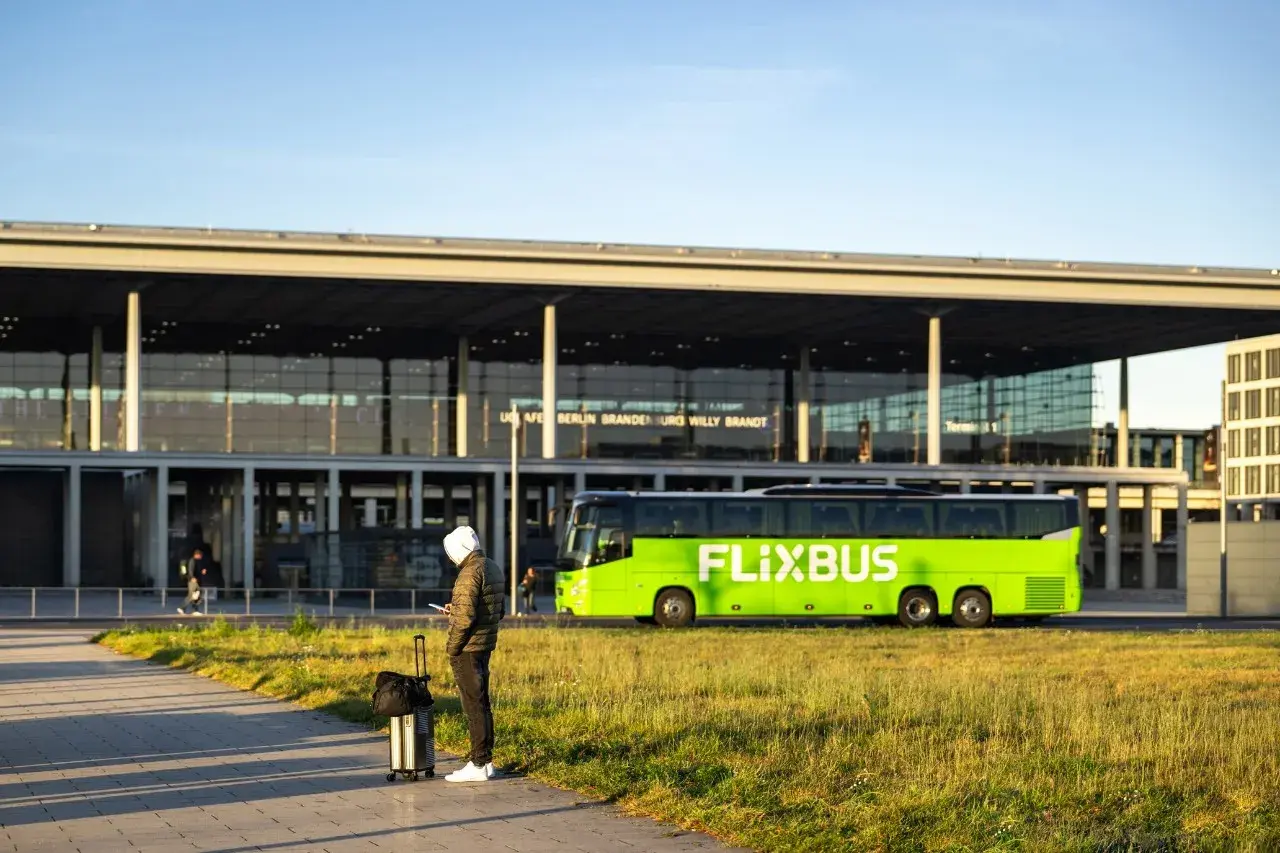 Mann mit Koffer wartet auf den Flixbus am Flughafen Berlin Brandenburg. Eine Direktverbindung Dresden Berlin Flughafen ist hier möglich.