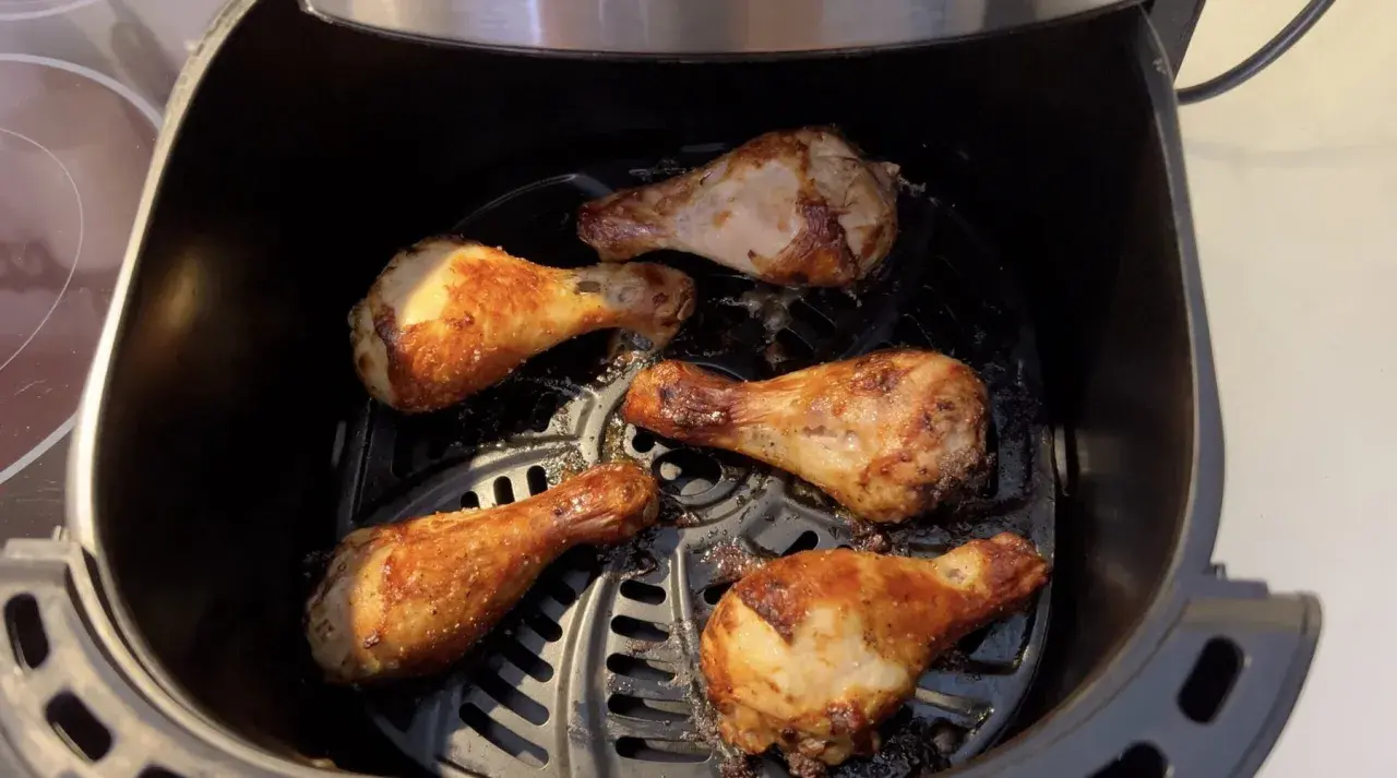 Cinq pilons de poulet dorés et croustillants cuisent dans une friteuse à air.