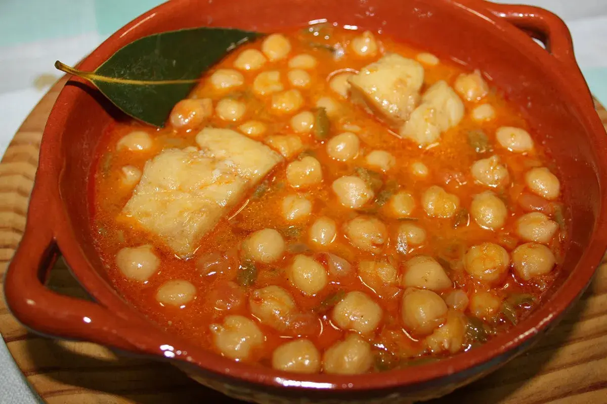 Garbanzos con bacalao, la receta de la abuela, servidos en cazuela de barro con hoja de laurel.
