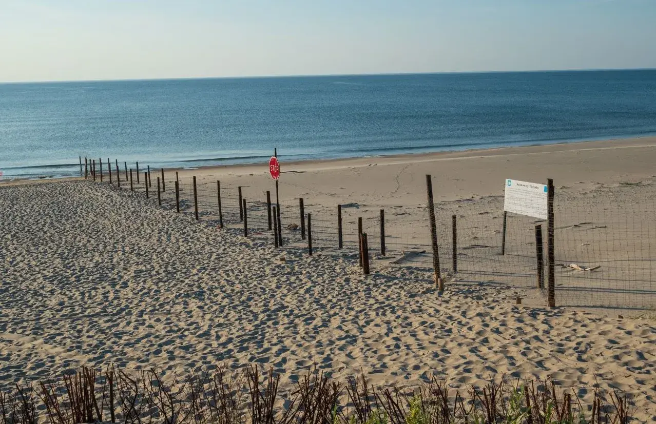 Plaża z siatką i znakiem stop, wyznaczająca granicę polsko rosyjską. Morze w tle.