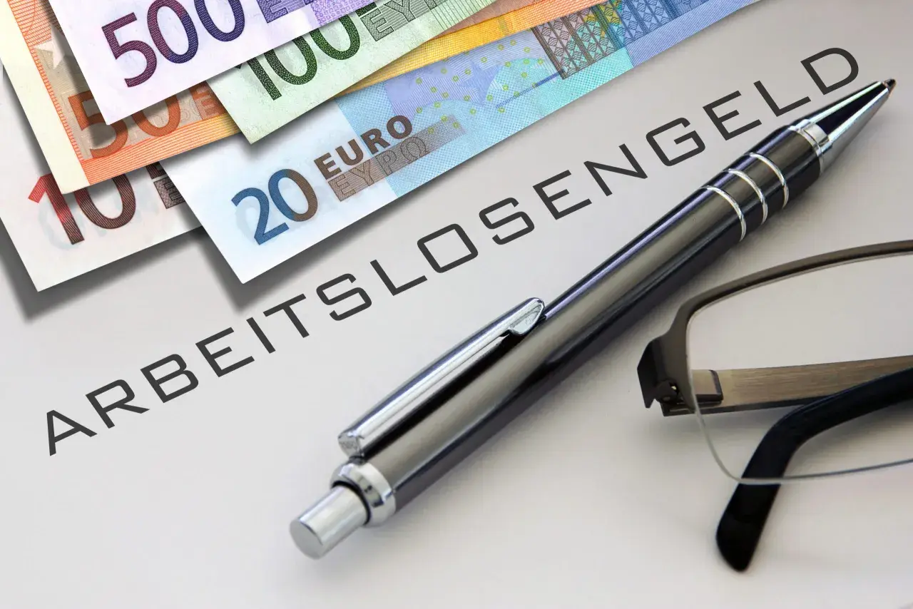 Euro-Scheine liegen neben einem Stift und einer Brille auf einem Dokument mit der Aufschrift "ABFINDUNG ARBEITSLOSENGELD".